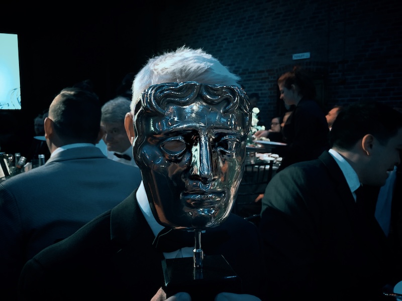 Bronze ceremonial mask figure among tuxedo-clad attendees, still from a Wise Media short