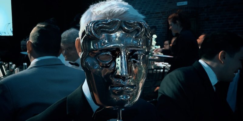 Bronze mask figure among black-tie guests, film still